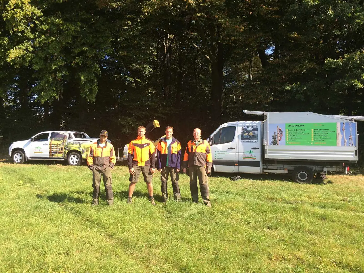 Das Team von Oliver Schäfer in Arbeitskleidung auf einer Wiese vor den Firmenfahrzeugen